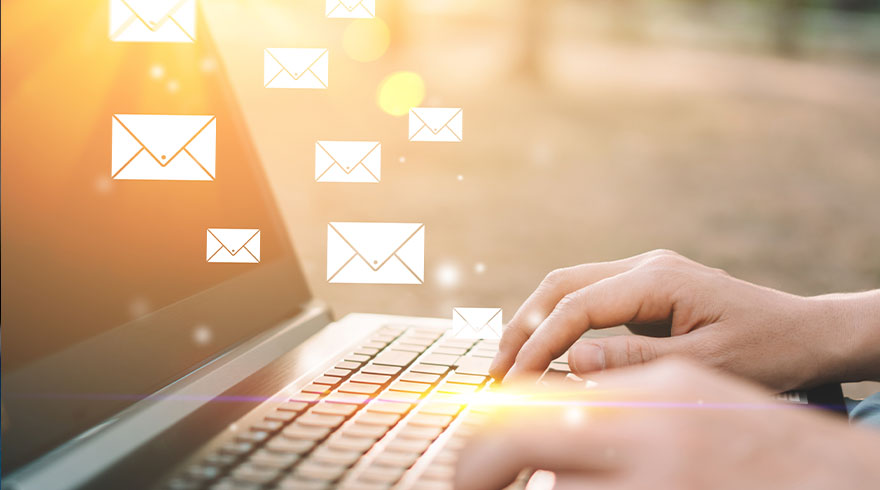 Typende handen op een laptop met witte envelop-pictogrammen die e-mail symboliseren, tegen een beige achtergrond.