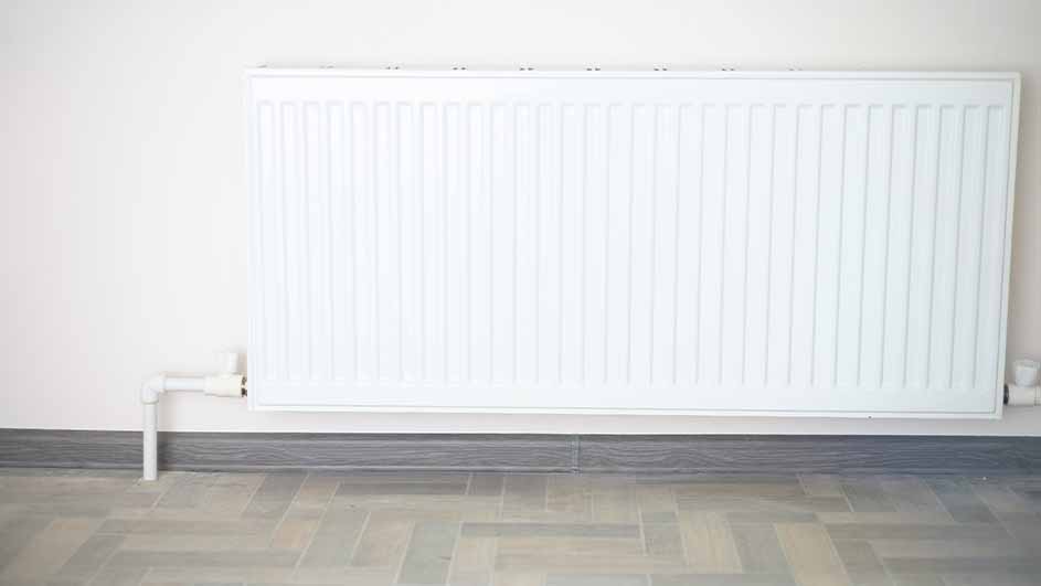 Een witte radiator hangt aan een crème muur, met grijze plinten en een grijze tegelvloer.