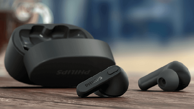 Zwarte draadloze Philips oordopjes en een open oplaadcase op een houten oppervlak, met een vage achtergrond.