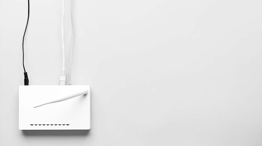 Een witte router met een antenne en aangesloten zwarte en witte kabels tegen een witte achtergrond.