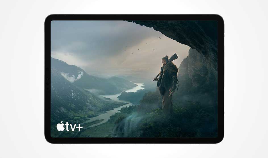 On a tablet, an Apple TV+ scene shows a lone hunter at a cave mouth, overlooking a foggy river valley between steep mountains.