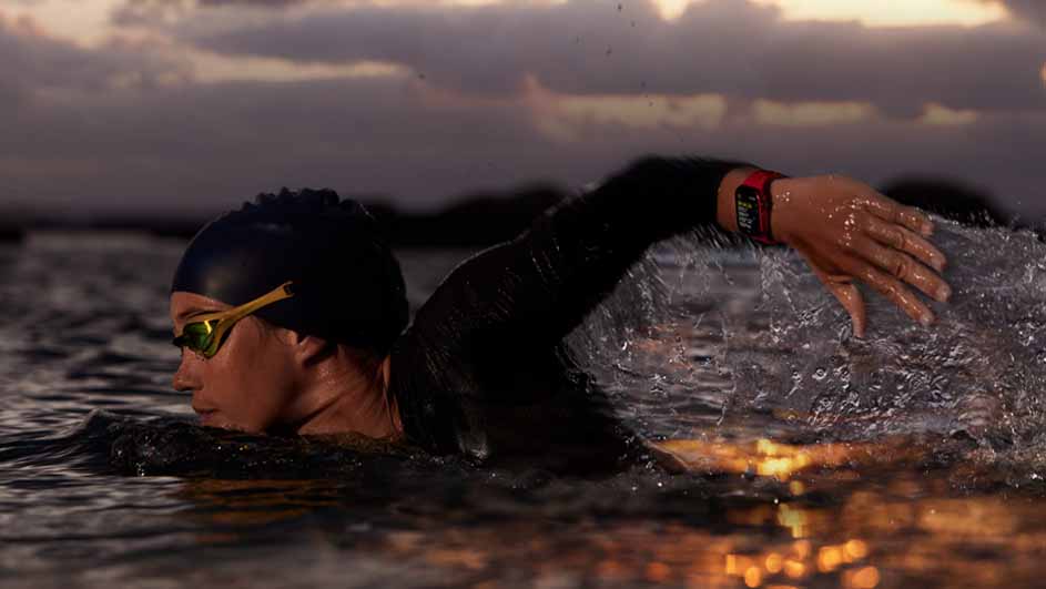 Een persoon zwemt in het water met een badmuts en een zwembril, terwijl het water rondom spat.