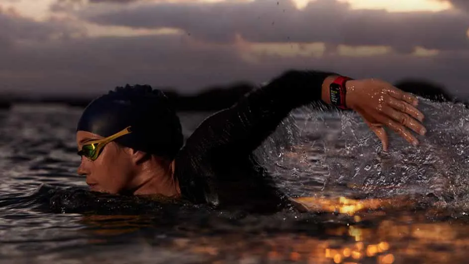 Een persoon zwemt in het water met een badmuts en een zwembril, terwijl het water rondom spat.