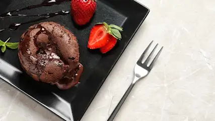 Chocolade fondant met aardbeien en een vork op een zwart bord, met chocoladesaus.