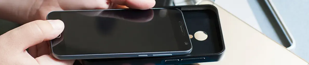 Hand houdt een zwarte smartphone boven een zwart telefoonhoesje op een licht oppervlak.