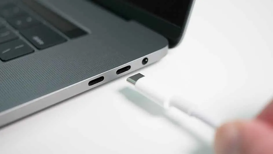 Een grijze laptop met een witte USB-C kabel die in een van de poorten wordt gestoken, op een witte achtergrond.