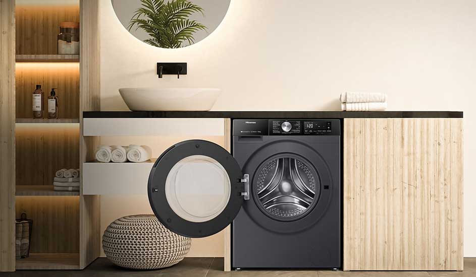 Een zwarte Hisense wasmachine met open deur staat in een moderne, lichte badkamer onder een wastafel en naast opgerolde handdoeken.