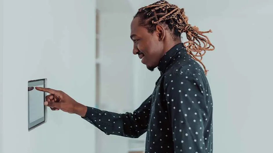 Een man met gevlochten haar bedient een aanraakscherm aan een witte muur. Hij draagt een zwart overhemd met witte stippen.