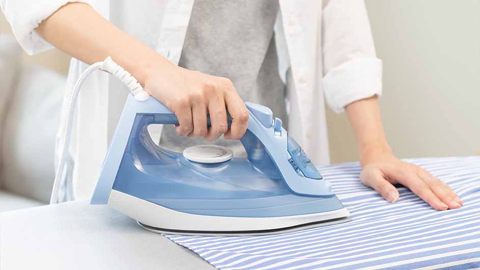 Een persoon strijkt een blauw-wit gestreept overhemd met een blauw strijkijzer op een strijkplank.