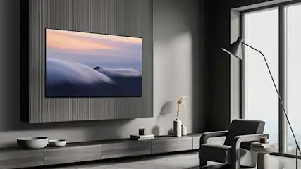 Minimalistisch interieur met een grote tv aan de wand. Grijze meubels, lange ramen en een vloerlamp geven het geheel een luxe uitstraling.