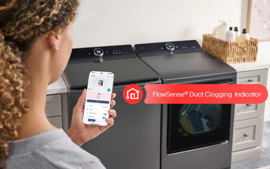 Vrouw gebruikt haar telefoon naast wasmachine en droger, met FlowSense-melding voor een mogelijk verstopt luchtkanaal.