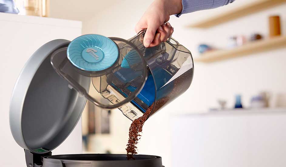 A hand empties the dust container of a Philips vacuum cleaner into a rubbish bin.