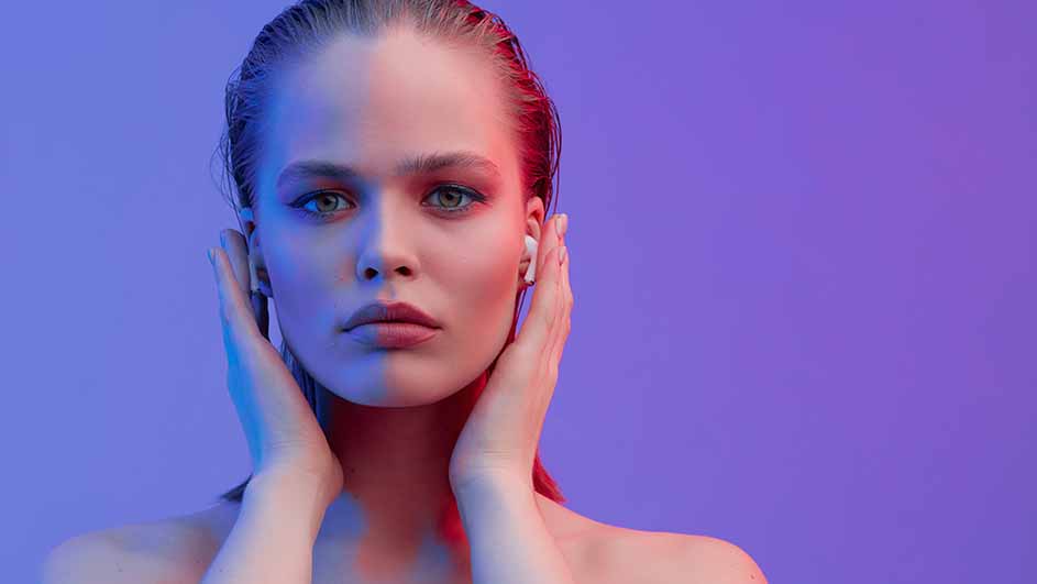 Vrouw met oortjes, handen bij oren, tegen een paarsblauwe achtergrond.