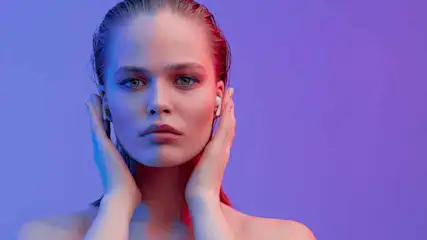 Vrouw met oortjes, handen bij oren, tegen een paarsblauwe achtergrond.