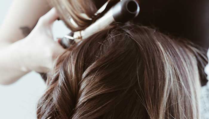 Een persoon krult bruin haar met een krultang. Het haar heeft lichte highlights en is in golven gestyled.