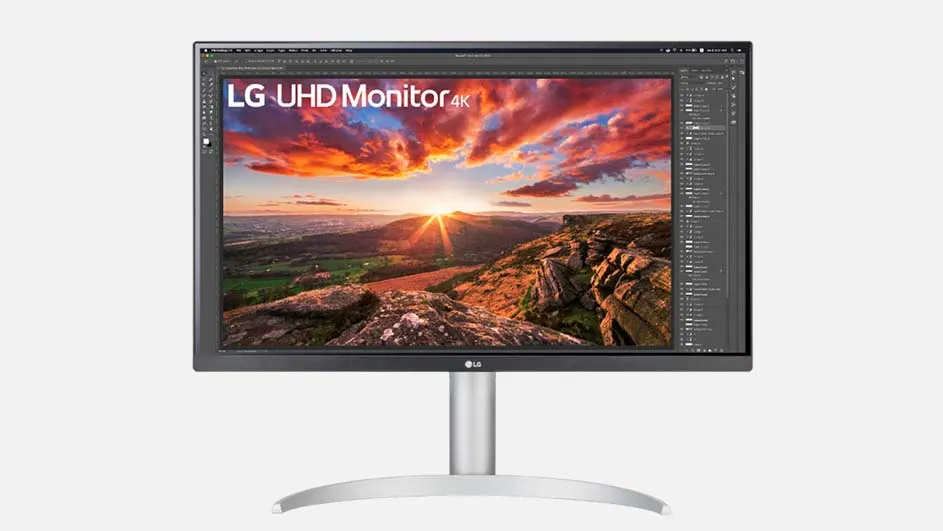 Een grijze LG UHD 4K monitor staat op een zilveren voet tegen een witte achtergrond. Het scherm toont een landschap met een zonsopgang.