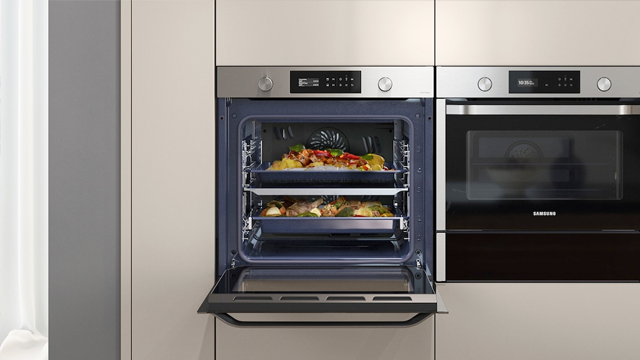 Oven met open deur toont twee bakplaten met voedsel, naast een gesloten oven in een beige keuken.