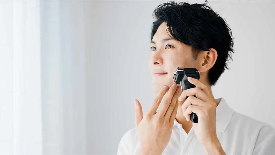 Een man scheert zich met een zwart elektrisch scheerapparaat tegen een witte achtergrond.