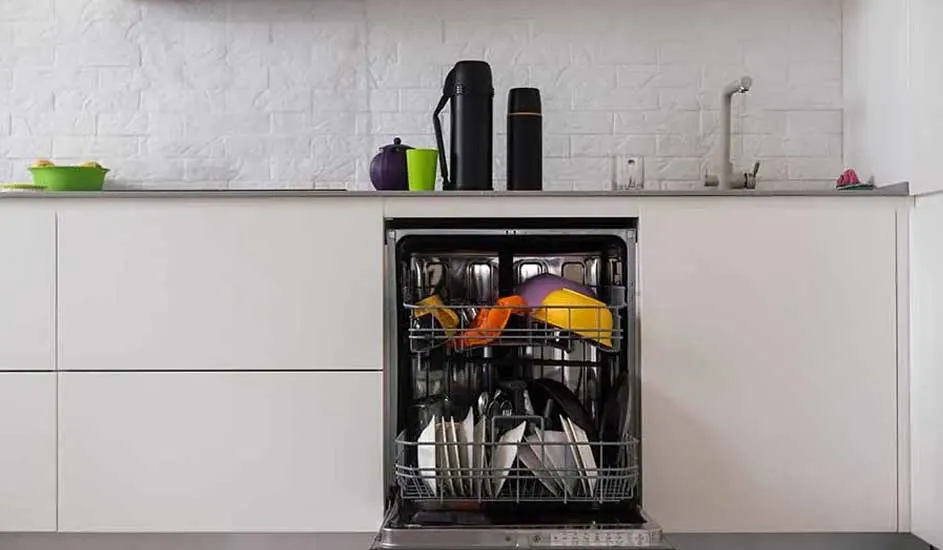 Een open vaatwasser vol met borden en gekleurde items in een witte keuken met een aanrecht vol spullen.
