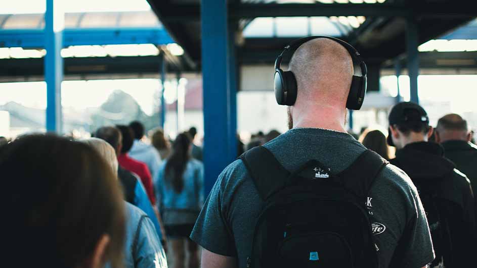 Kale man met rugzak en noise-cancelling koptelefoon in een druk treinstation of busstation.