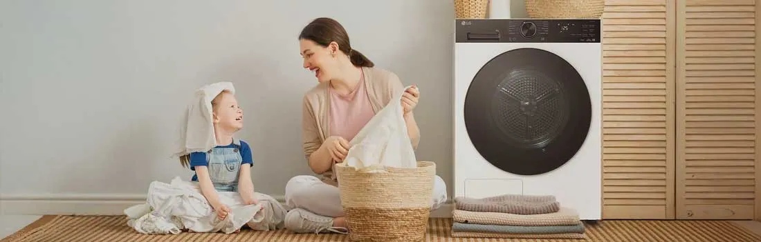 Een moeder en kind zitten lachend bij de wasmand naast een moderne wasmachine, met gevouwen handdoeken en houten kasten erbij.