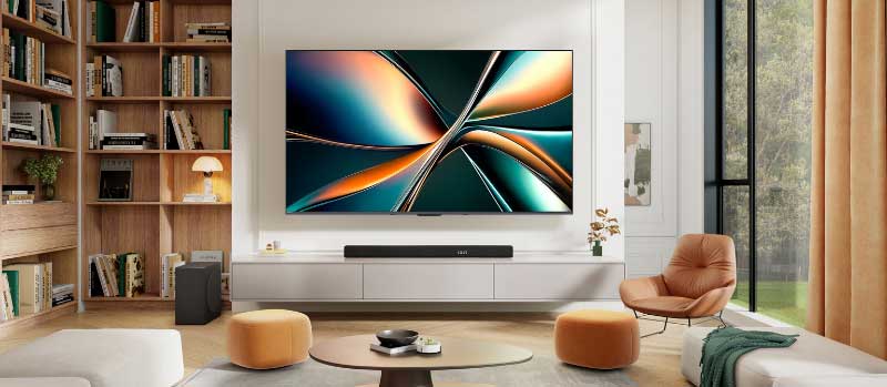 Een gezellige woonkamer met grote tv, soundbar, boekenkast, fauteuil, poefs en hoge ramen met gordijnen in warme moderne stijl.