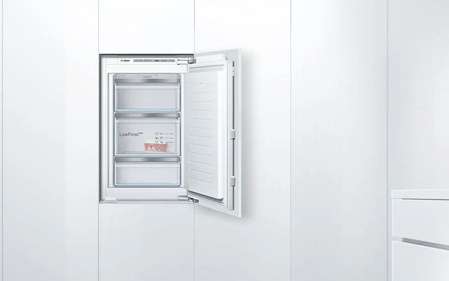 Witte inbouwvriezer in een strakke keukenwand, deur open zodat drie transparante lades met LowFrost-label en voedselverpakking zichtbaar zijn