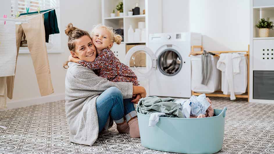 Een vrouw met een kind in de wasruimte, omhelzend naast een wasmand en een wasmachine.