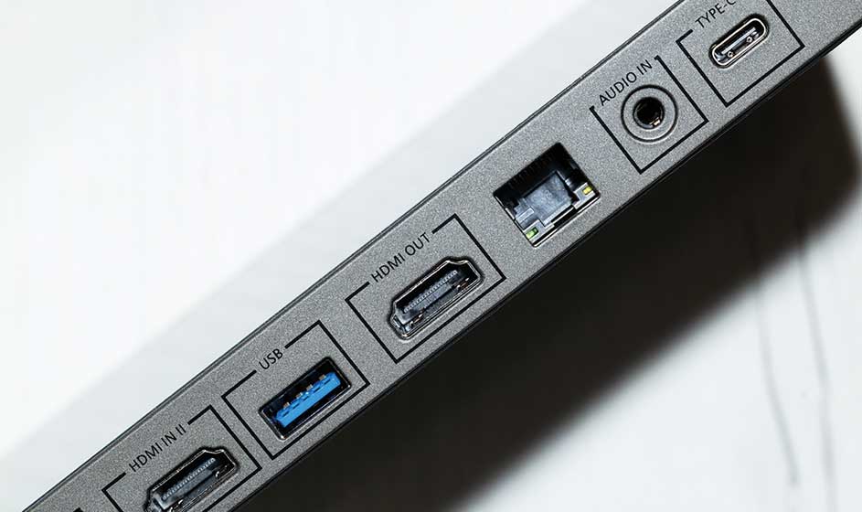 Aansluitingen op een grijs apparaat zijn zichtbaar: HDMI, USB, LAN en audio; alles oogt strak en technisch gefotografeerd.