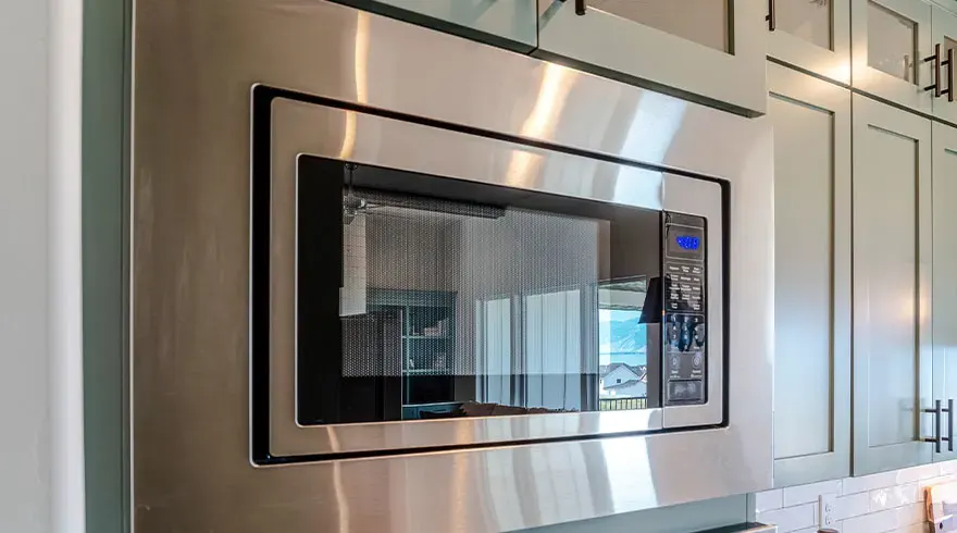 Roestvrijstalen magnetron ingebouwd in een grijze kast met zwarte handgrepen in een keuken.