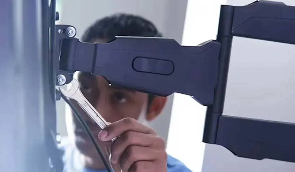 A person is mounting a television to an adjustable, extendable wall bracket in a bright room with a modern appearance
