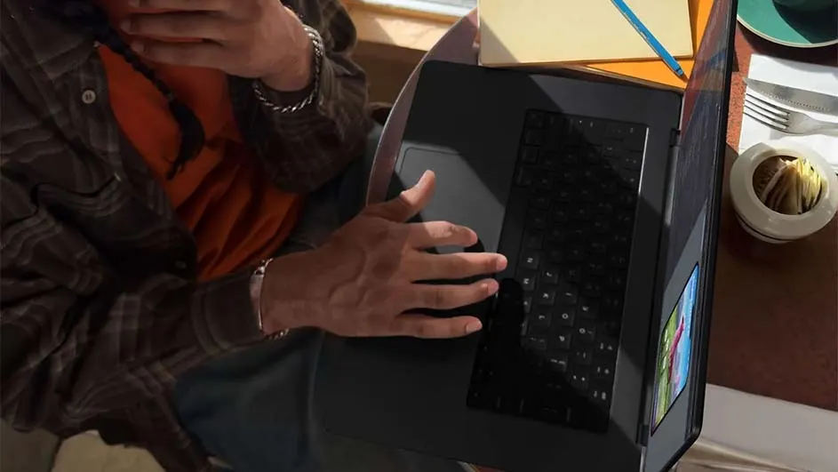 Person using a black laptop with a utensil holder, fork, and knife on a brown table. Sticky notes and a blue pen are visible.