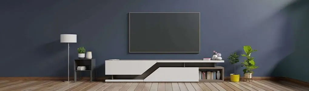 Een woonkamer met een blauwe muur, een tv, een witte kast, een lamp, planten en een houten vloer.