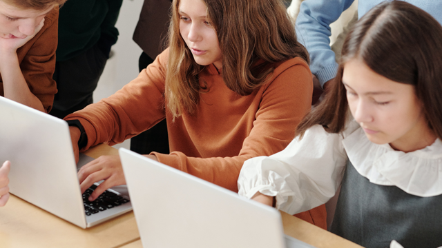 Jonge mensen werken aan laptops op een tafel. Ze dragen verschillende kledingstukken.