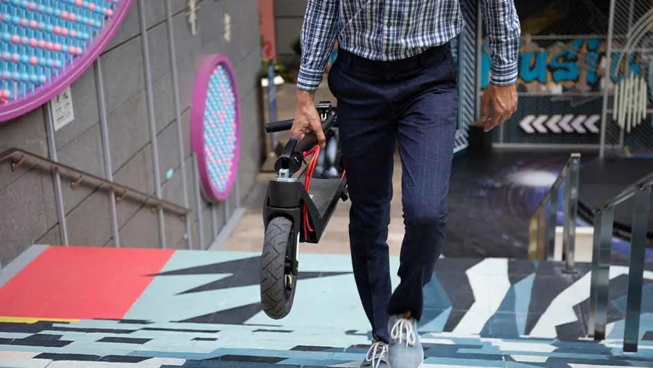 Een persoon draagt een opvouwbare scooter de trap af in een stedelijke omgeving met kleurrijke muurschilderingen.