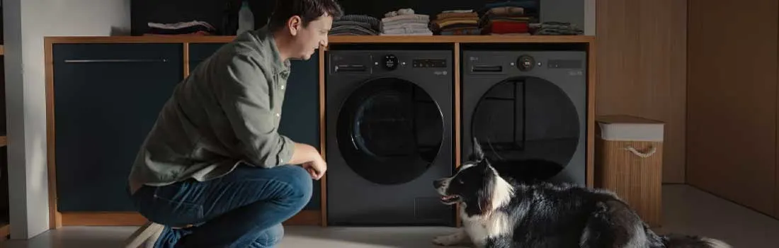 Man knielt in een nette wasruimte naast een hond, voor donkere LG wasmachines en opgevouwen wasgoed op planken.