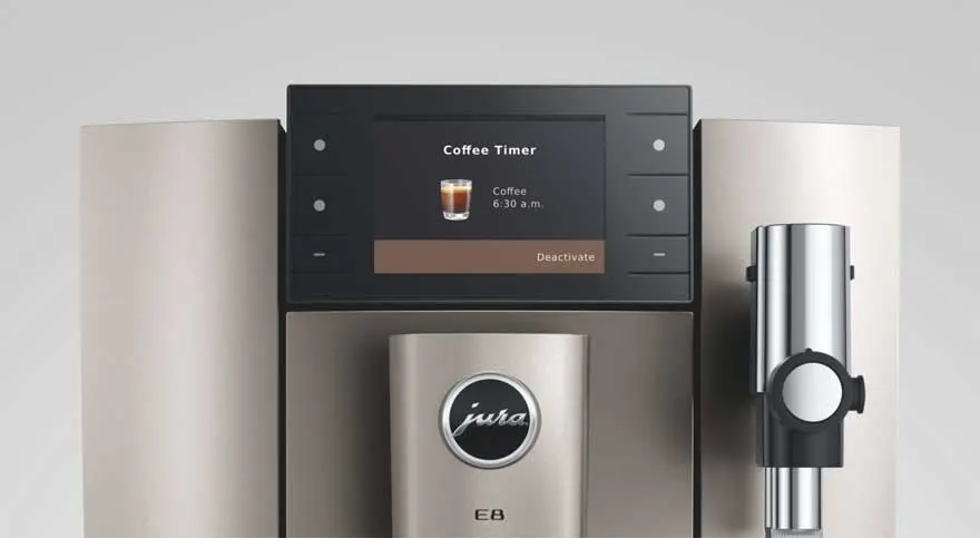 Close-up van een Jura E8 koffiemachine: centraal het display met ‘Coffee Timer’, onder het logo, rechts een melkopschuimer.