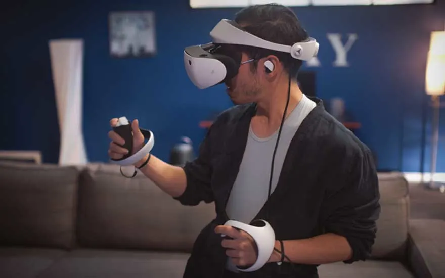 A gamer wearing a VR headset holds two motion controllers, standing before the sofa and fully immersed in a vivid virtual world.