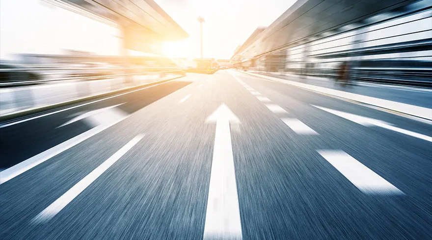 Een blauwe weg met witte pijlen leidt naar een horizon met gebouwen en een heldere lucht.