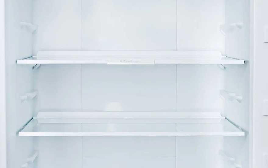 Close-up van een open, volledig lege koelkast met drie glazen legplanken, helder wit en klaar om opnieuw ingeruimd te worden
