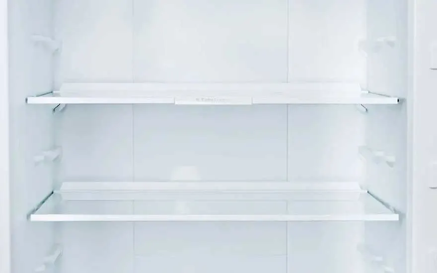 Close-up van een open, volledig lege koelkast met drie glazen legplanken, helder wit en klaar om opnieuw ingeruimd te worden