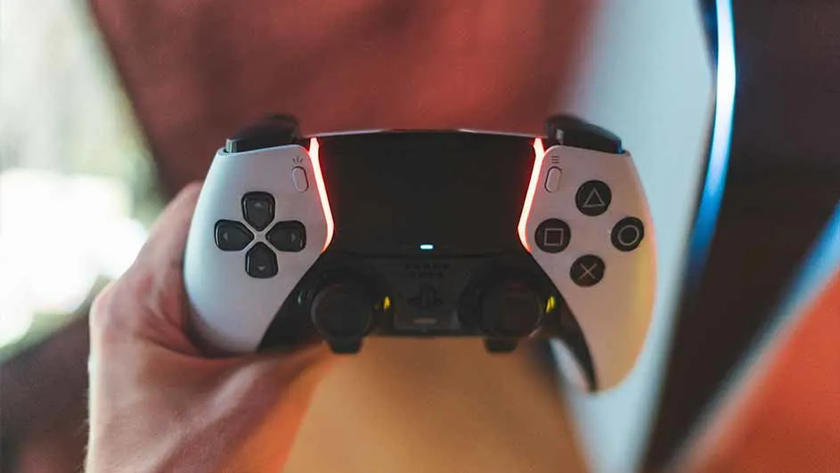 Een hand houdt een witte en zwarte PlayStation-controller vast met knoppen, sticks en een blauw licht.