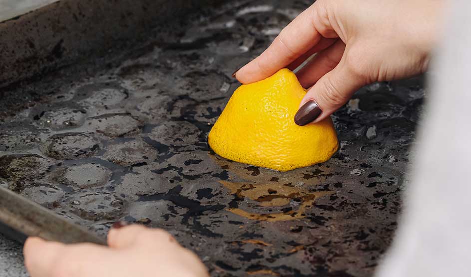 Someone scrubs a greasy baking tray with half a lemon, a natural way to loosen grime.