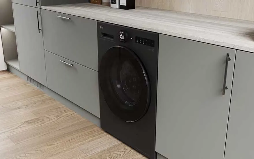 Zwarte LG wasmachine geïntegreerd onder een werkblad tussen grijsgroene kasten, in een strakke moderne bijkeuken.