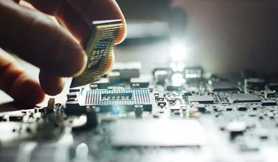 Close‑up of a hand gently placing a computer processor onto a motherboard, surrounded by tiny gleaming electronic components.