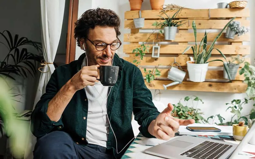 Man drinkt koffie terwijl hij aan zijn laptop werkt met planten en accessoires op de achtergrond.