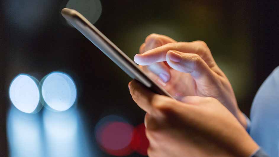 Handen bedienen een smartphone tegen een donkere achtergrond met wazige lichten.