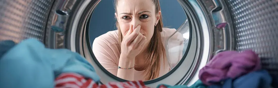 Een blik vanuit de binnenkant van een wasmachine. Iemand kijkt met een afkeurende blik naar binnen en houdt de neus dicht vanwege een onaangename geur.