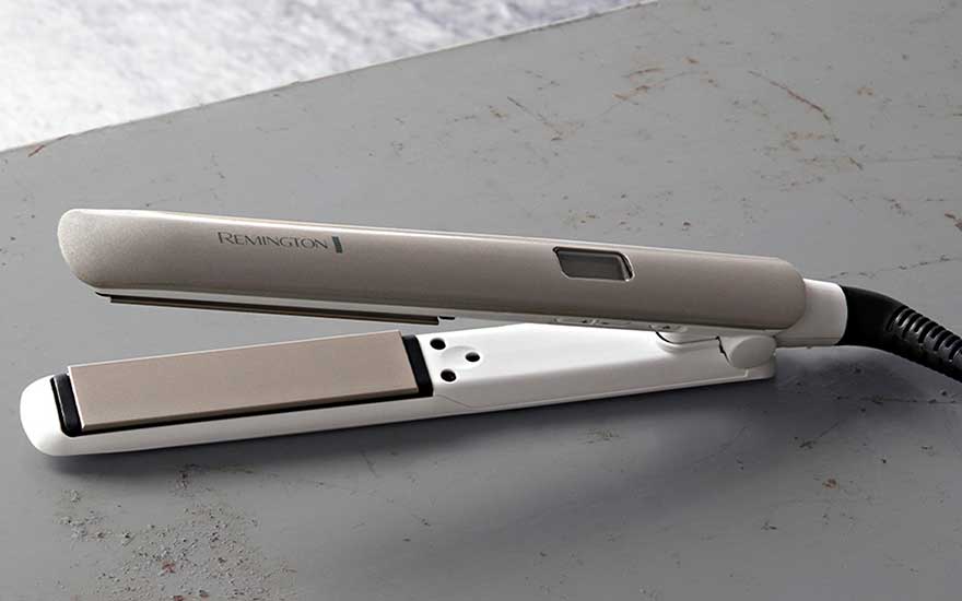 Een witte Remington-stijltang ligt open op een grijze tafel, met de platen zichtbaar en het snoer aan de rechterkant.