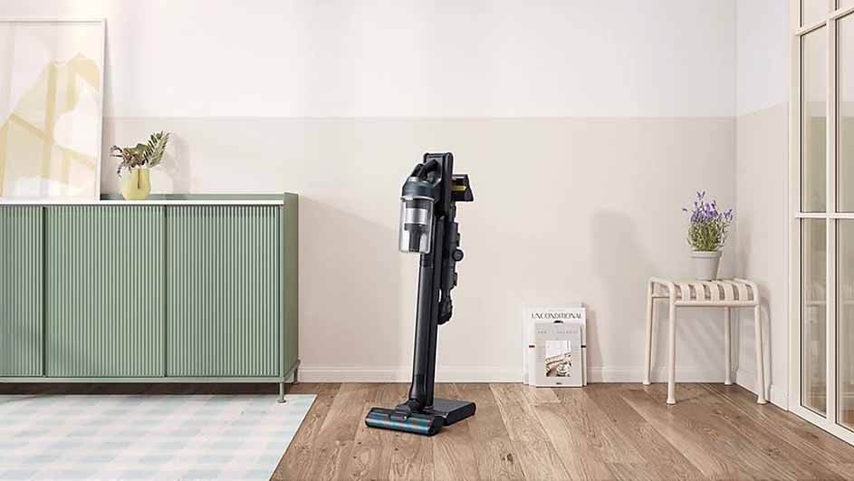 Een zwarte stofzuiger staat op een houten vloer in een kamer met een kast en een krukje.